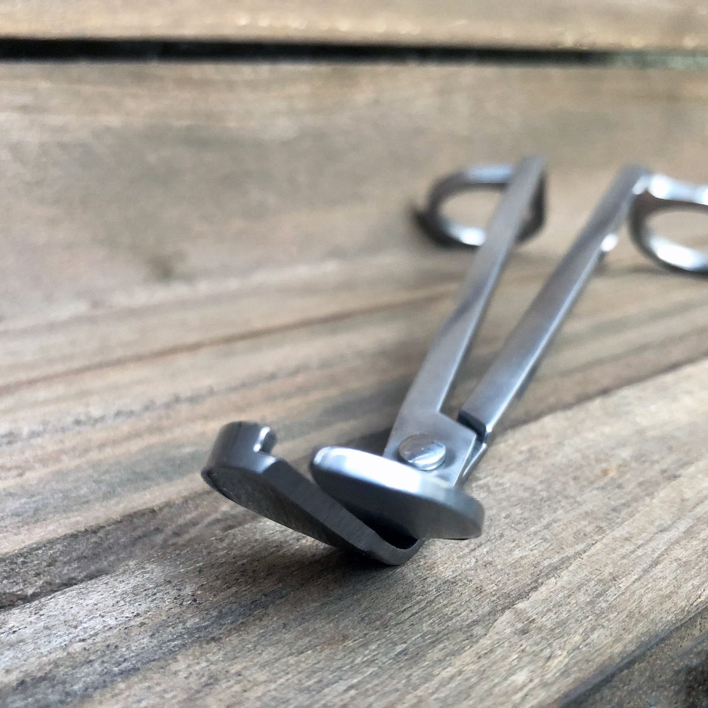 Stainless steel candle wick trimmers against weathered wood background.