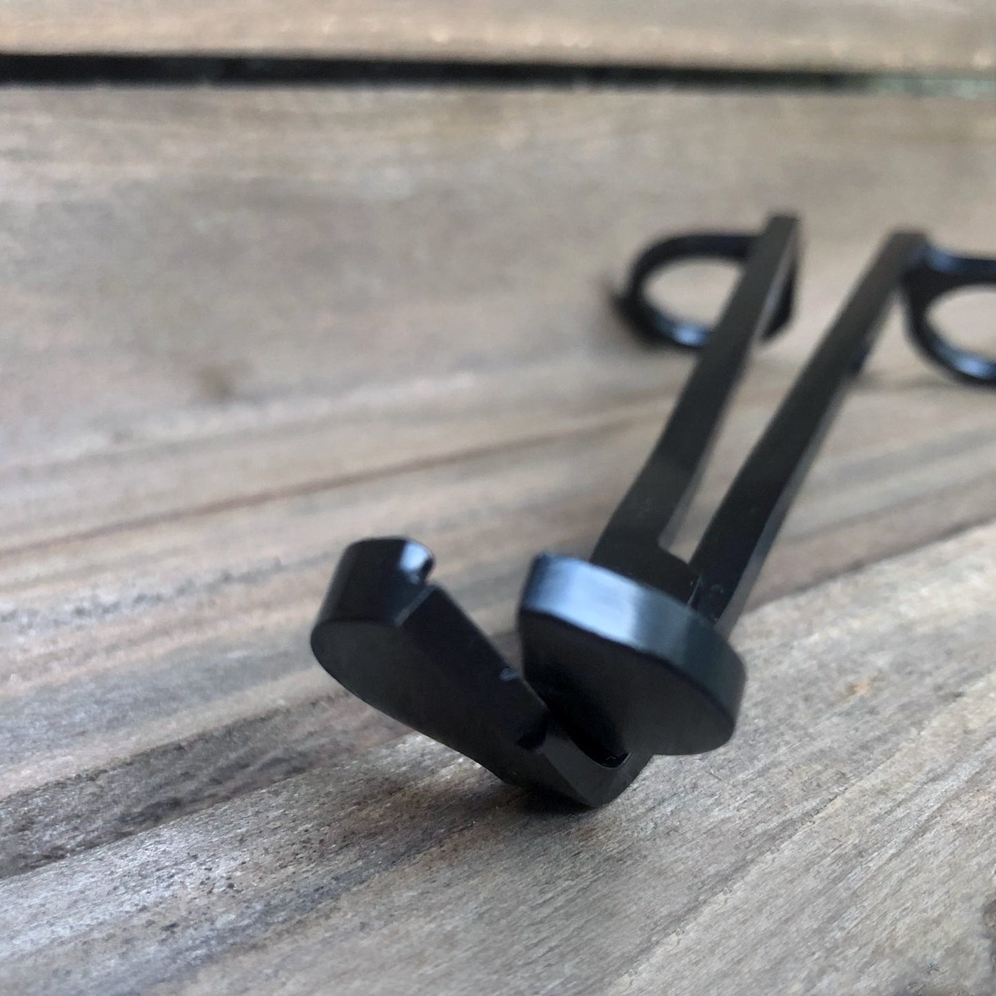 Wickman matte black candle wick trimmers against weathered wood background.