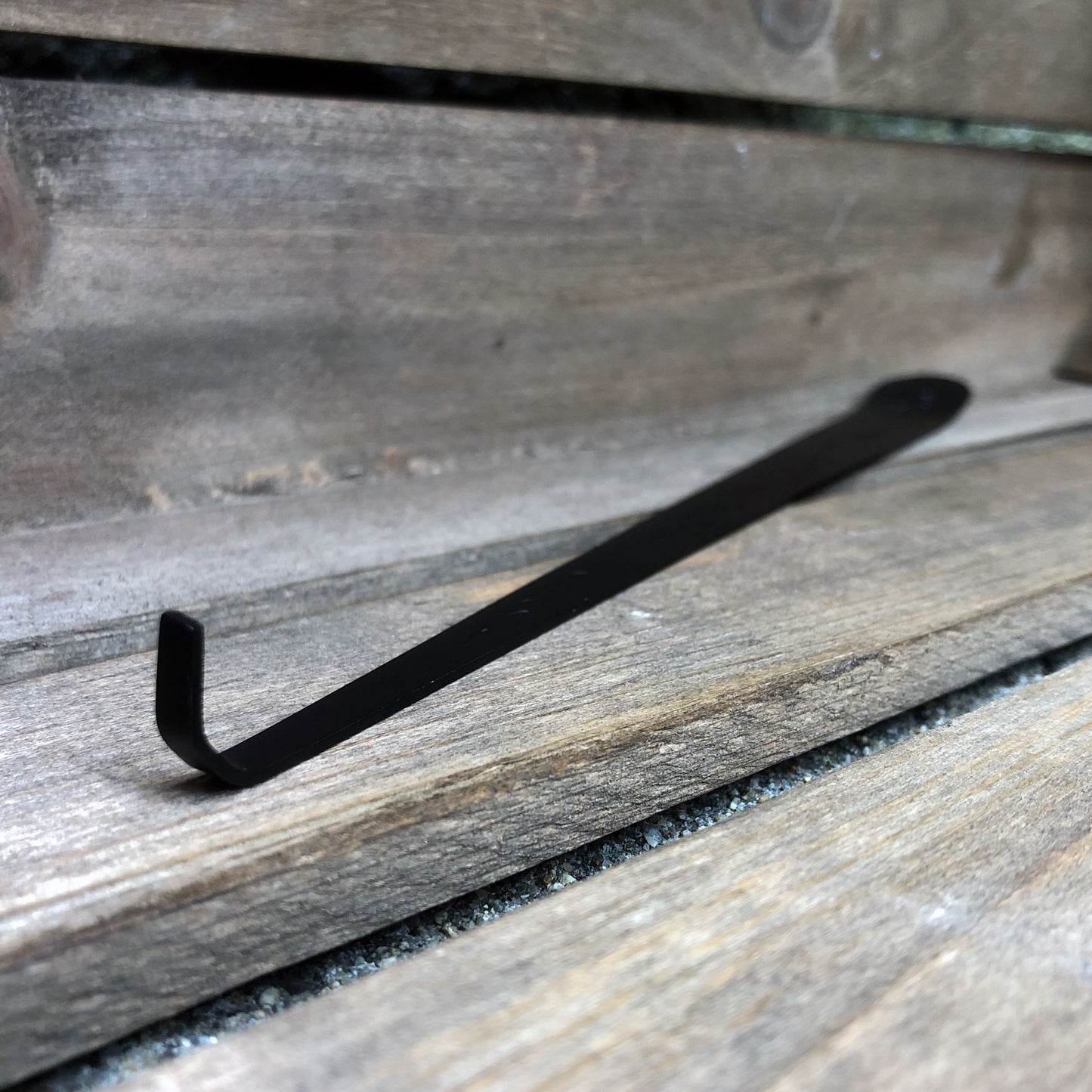 Matte black, smokeless candle wick dipper against a weathered wooden crate.