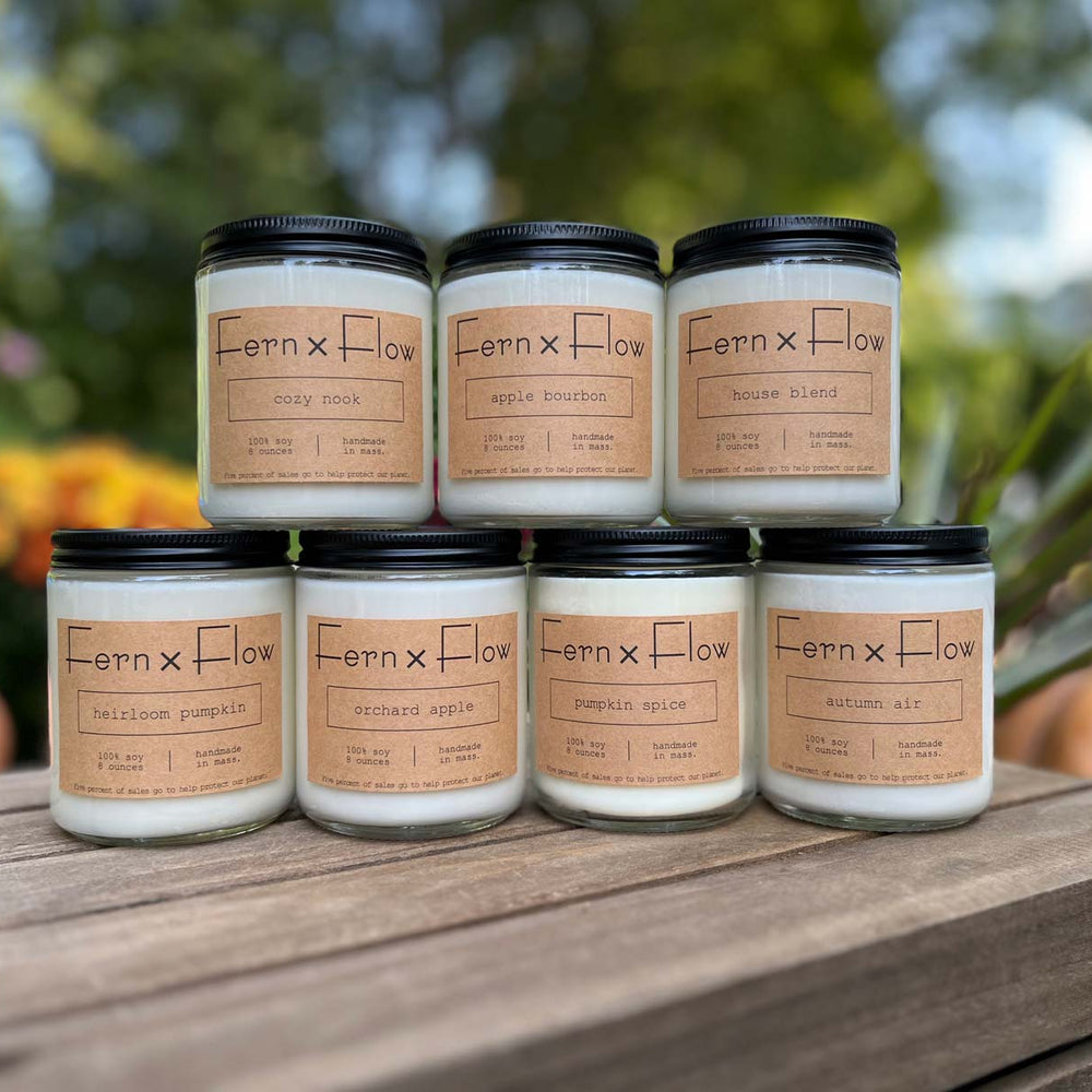 Fern x Flow hand-poured autumn candle collection on a weathered, wooden crate with mums and pumpkins in the background,