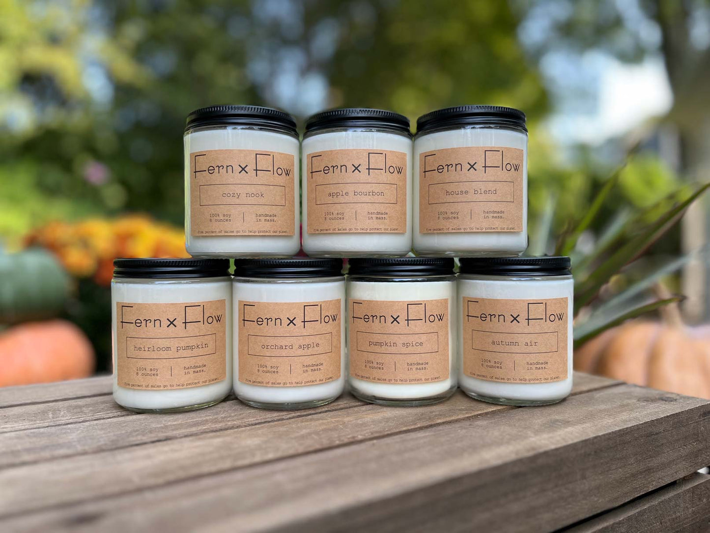 Fern x Flow hand-poured autumn candle collection on a weathered, wooden crate with mums and pumpkins in the background,