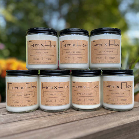 Fern x Flow hand-poured autumn candle collection on a weathered, wooden crate with mums and pumpkins in the background,