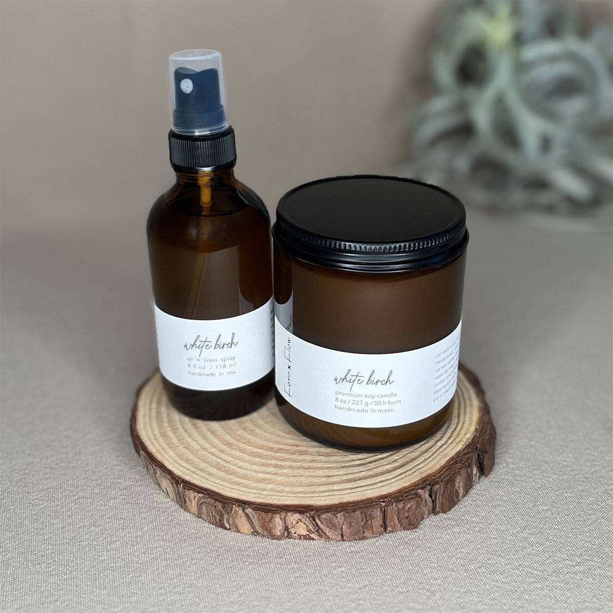 Fern x Flow Oakmoss + Amber scented soy candle and Air + Linen Spray bundle on a wooden riser.