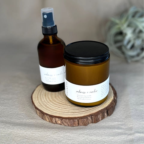 Fern x Flow Oakmoss + Amber scented soy candle and Air + Linen Spray bundle on a wooden riser.