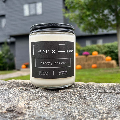 Fern x Flow Sleepy Hollow Halloween scented soy candle with a black and white label in front of The Salem Witch House in Salem MA
