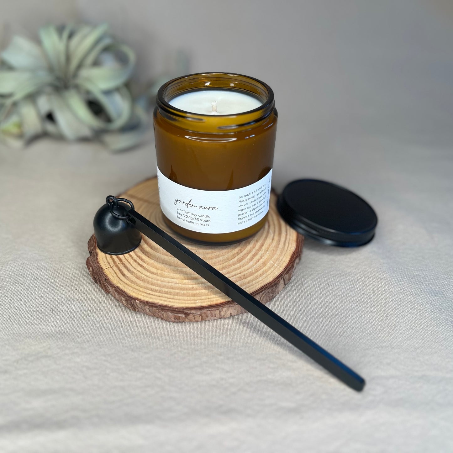Eight-ounce Fern x Flow Garden Aura scented soy candle with matte black candle wick trimmers.Eight-ounce Fern x Flow Garden Aura scented soy candle with a matte black candle snuffer.