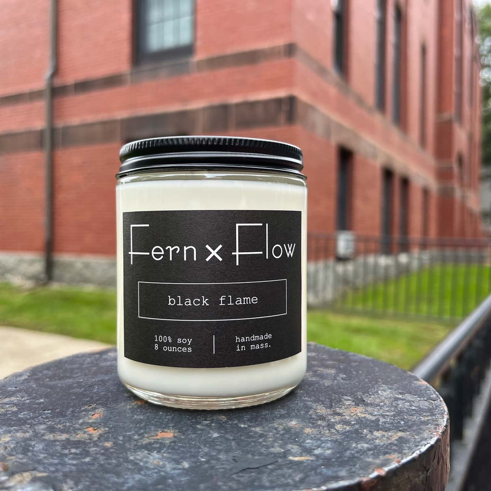 Fern x Flow Black Flame Halloween scented soy candle in front of brick building in Salem, MA