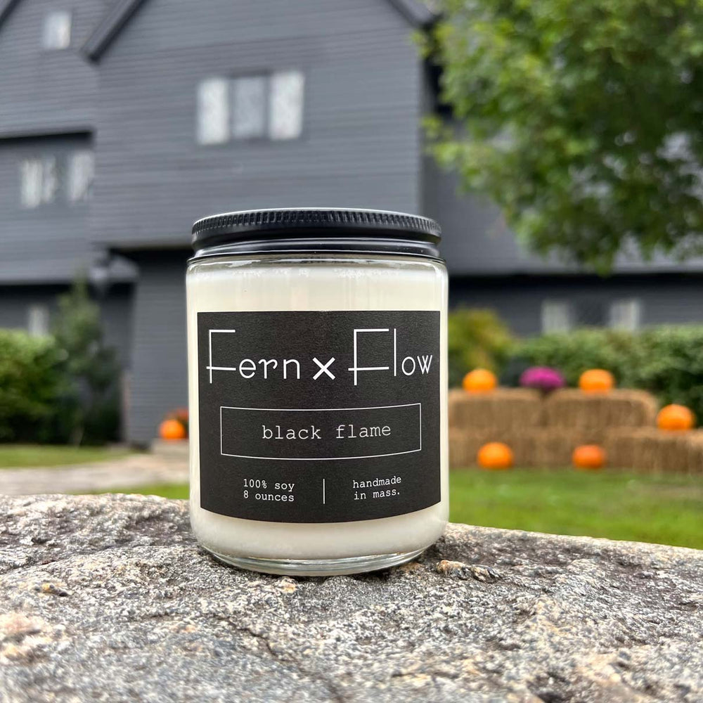 Fern x Flow Black Flame Hocus Pocus-inspired Halloween soy candle with a black and white label in front of The Salem Witch House in Salem MA