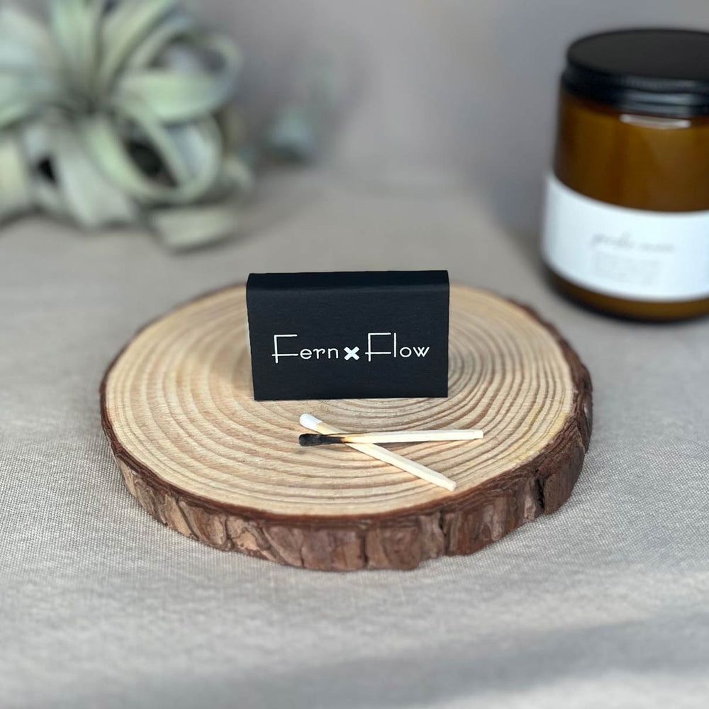 Fern x Flow matte black classic match box with white-tipped safety matches with a Fern x Flow candle in the background.