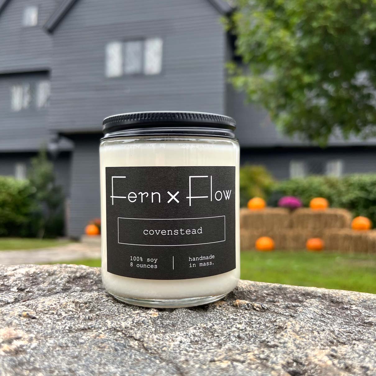 Fern x Flow Covenstead Halloween soy candle with a black and white label in front of The Salem Witch House in Salem MA
