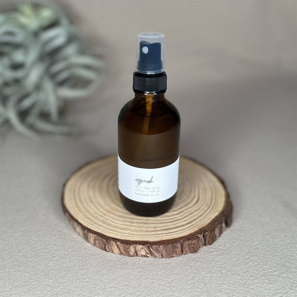 Fern x Flow Cozy Nook natural and vegan air and linen spray on a rustic wooden rise with air plant out-of-focus in the background.