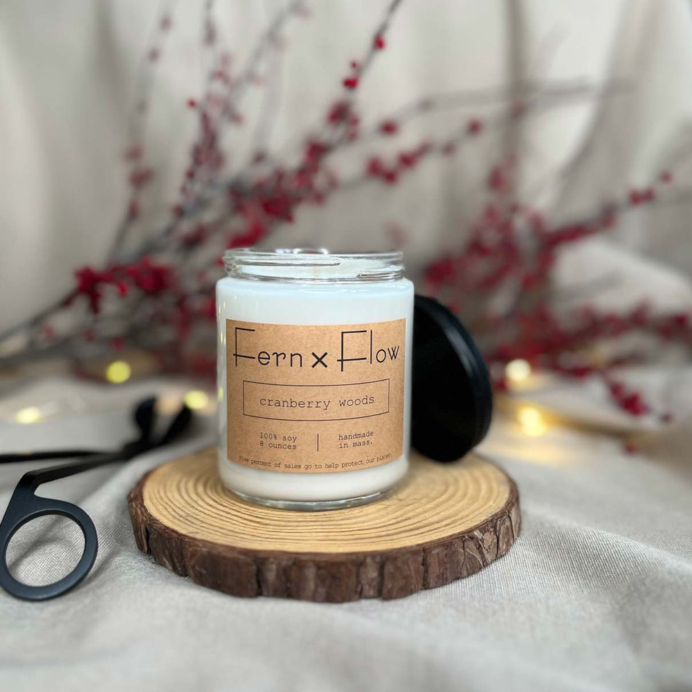 Eight-ounce Fern x Flow Cranberry Woods scented soy candle against a cream-colored cloth background with red berries