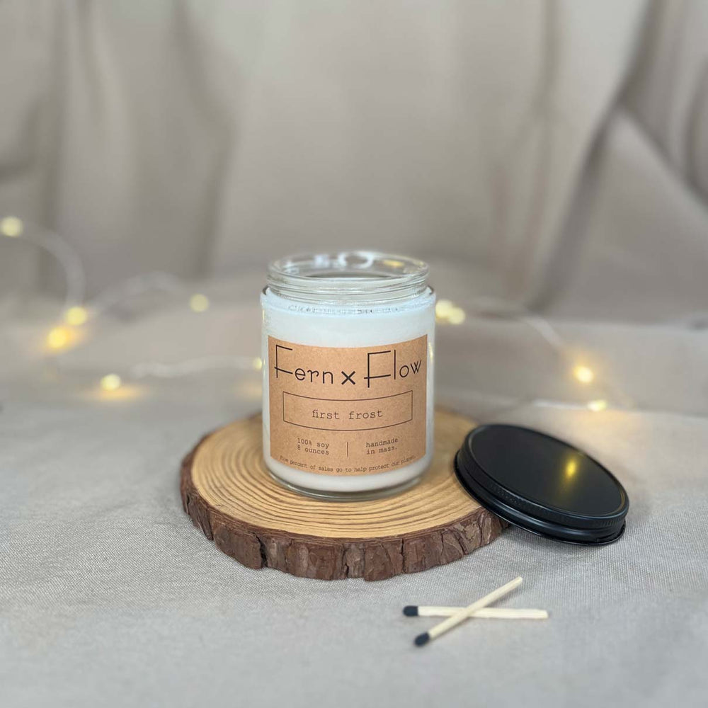 Eight-ounce Fern x Flow First Frost scented soy candle against a cream-colored cloth background with white Christmas lights.