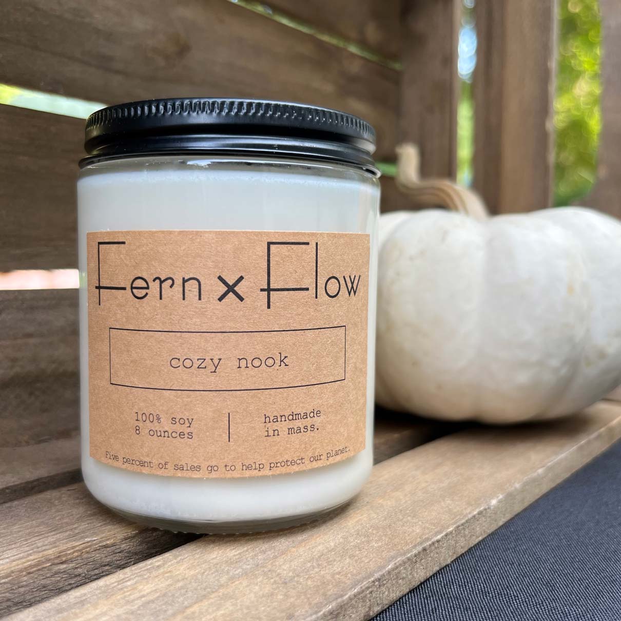 Fern x Flow Cozy Nook scented soy candle in a weathered, wooden crate with a small white pumpkin in the background.