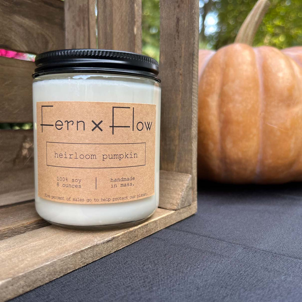 Fern x Flow Heirloom Pumpkin scented autumn soy candle on a weathered, wooden crate in front of an orange-y brown heirloom pumpkin.
