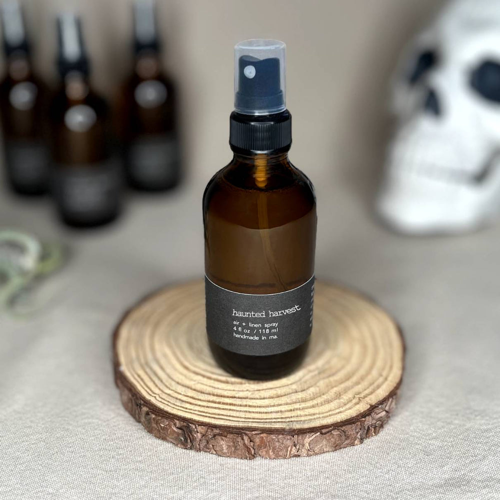Fern x Flow Haunted Harvest vegan Air + Linen spray on a rustic wooden riser in front of more out-of-focus sprays and a halloween skull decoration.