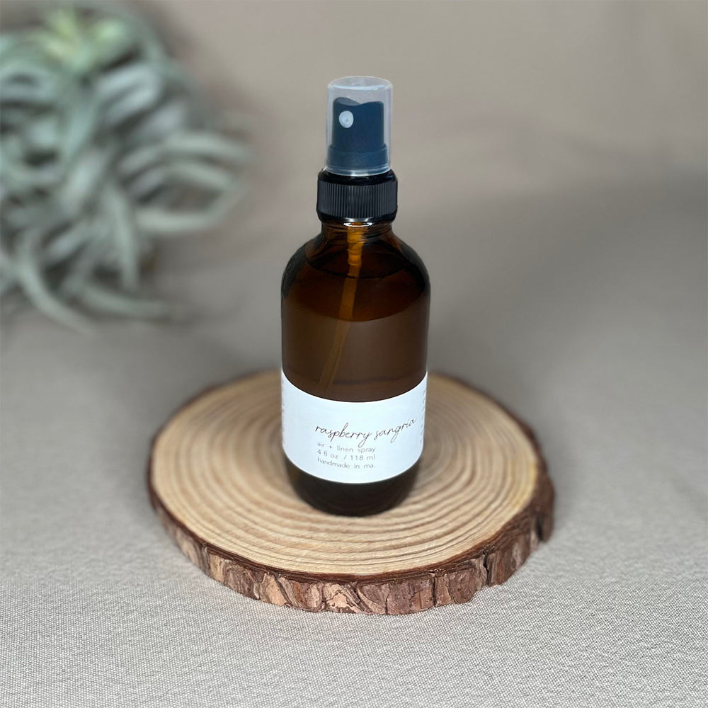Fern x Flow 4oz natural and vegan Raspberry Sangria scented Air + Linen Spray on a rustic wooden riser with large air plant out-of-focus in the background.