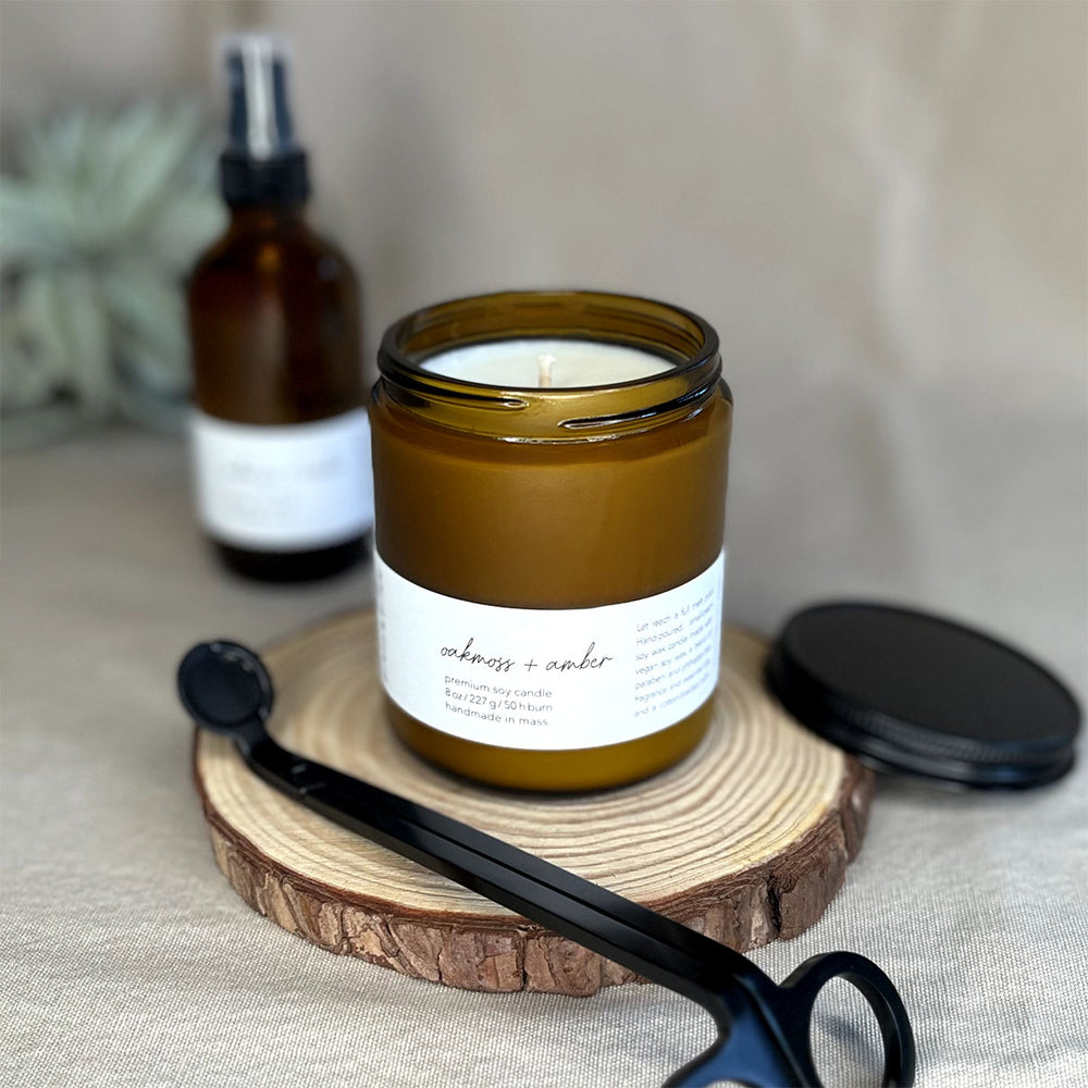 Fern x Flow Oakmoss + Amber vegan soy candle and air + linen spray fragrance bundle on a rustic wooden riser.