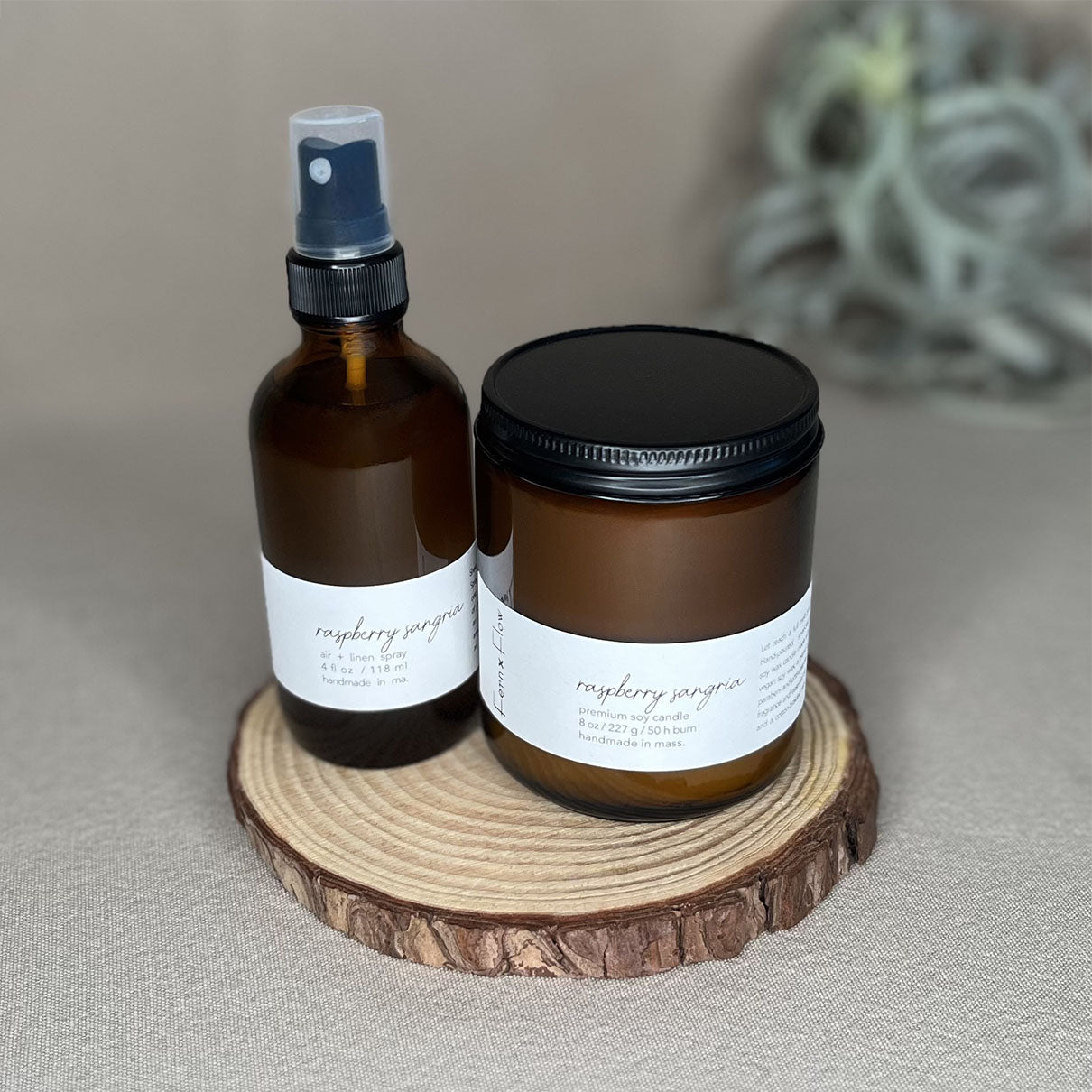 Fern x Flow Raspberry Sangria soy candle and air + linen spray fragrance bundle on a wooden rise in front of a large out-of-focus air plant in the background.