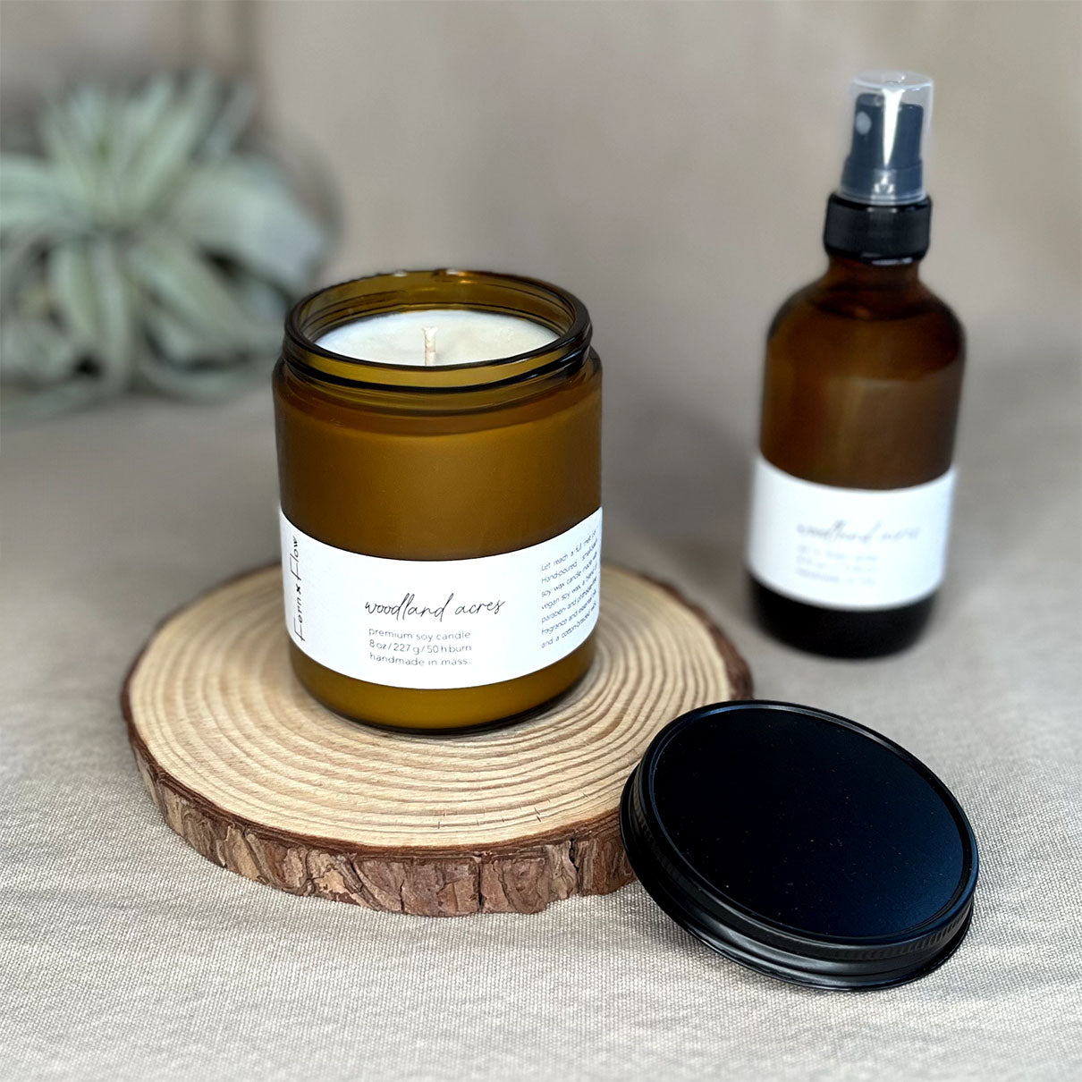 Fern x Flow Woodland Acres vegan soy candle and air + linen spray fragrance bundle on a rustic wooden riser.