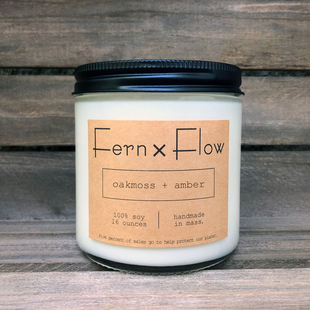 Sixteen-ounce Fern x Flow Oakmoss + Amber scented soy candle against a weathered, wooden crate.