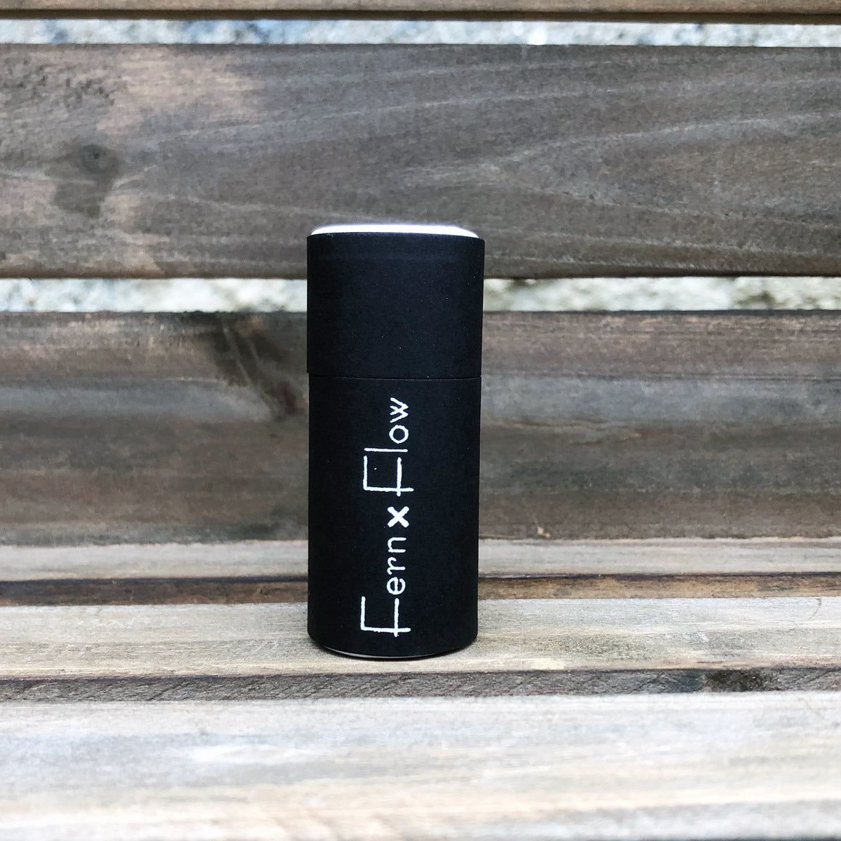 Fern x Flow, matte black, safety barrel match stick bottle against a weathered, wooden background.