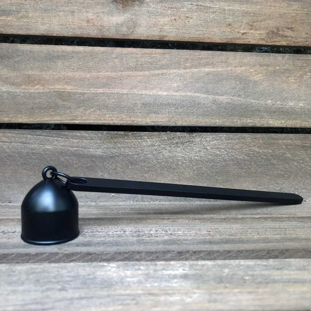Matte black candle snuffer against weathered wood background.