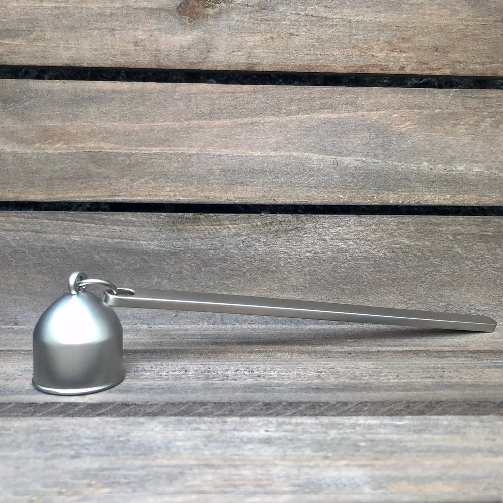 
                  
                    Stainless steel candle snuffer against weathered wood background.
                  
                